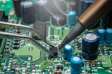 Close-up of a technician's hands in a workshop. The repairer is soldering an IC in a SOIC package...