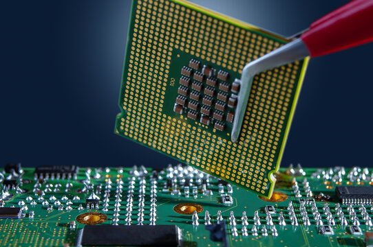 A technician holds a CPU chip in an LGA package with tweezers over an electronic circuit board.