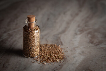 A small glass bottle filled with organic Carom seeds (Trachyspermum ammi) or Ajwain is placed on a marble background.