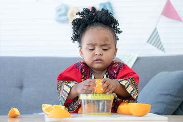 African cute kid girl squeezing fresh oranges with serious face at home. Adorable child intent to...