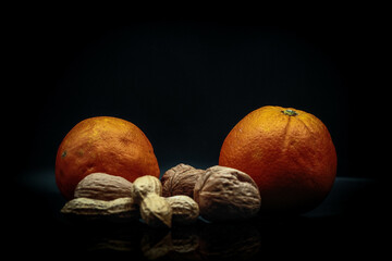 studio photo on black background of fresh and dried fruit. oranges, peanuts and walnuts in an...