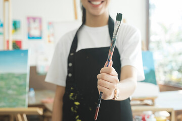 A close-up of the artist hands wearing an apron smeared with paint. Clutching many brushes and paintbrushes.