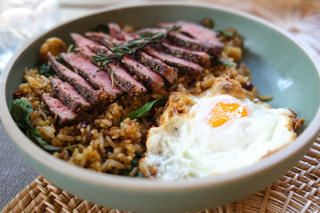 Blurred of Beef basil fried rice dish served with grilled Medium Rare beef and undercooked fried eggs