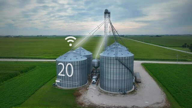 Futuristic farm with silos with animation of IoT connectivity and digital readouts. Farmer in USA selling corn at modern grain bin. Aerial with 3D render.