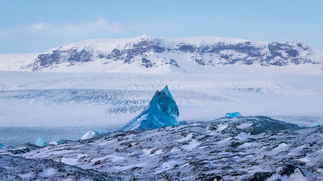 Blue ice fragment at Jokulsarlon Glacier Lagoon in Iceland with snow covered mountains in the background
