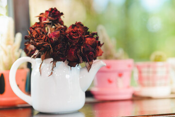 Dried dark red roses in a white vase on a wooden table in a home. Home decoration ideas.