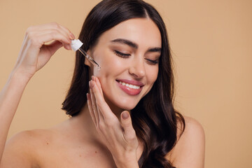 Woman Dropping Serum on Face on Beige Background