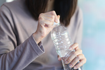 A woman tries to open the cap of a water bottle to drink.