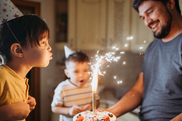 Boy wearing party hat and blowing candle on cake with family