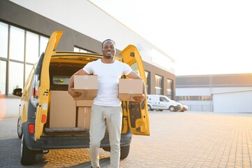 Portrait of a young African American package delivery man near a car with boxes.