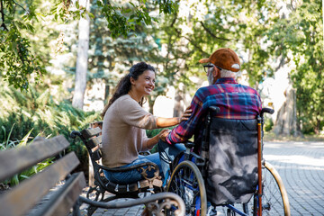 Smiling caregiver consoling retired senior man in wheelchair at park