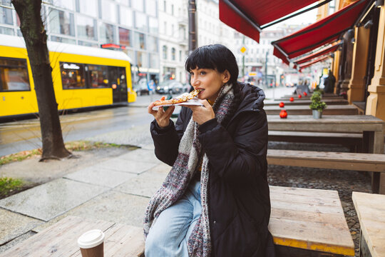 Woman eating pizza at sidewalk cafe
