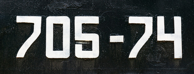 Weathered numbers 7, 0; 5, 4, seven, zerro, five, four, or 70574 painted white on a piece of black...