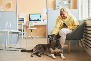 Smiling woman holding smart phone and petting dog in veterinary clinic
