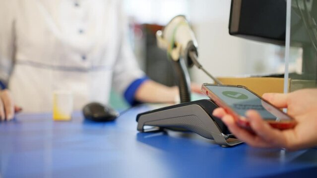 Close-up of a woman paying for medicine by phone in a pharmacy. Bank payment at the cash register, work of a pharmacist. High quality 4k footage