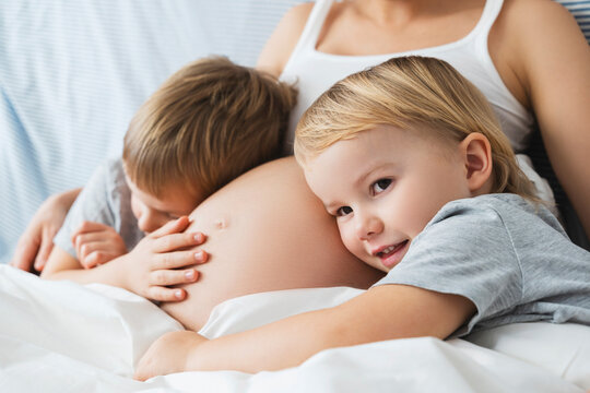 Happy children leaning on pregnant mother's stomach at home