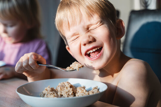 Cheerful boy eating porridge for breakfast at home