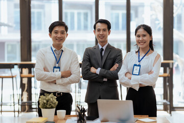 Young asian business people posing with their arms crossed in the office smiling and looking at the camera.