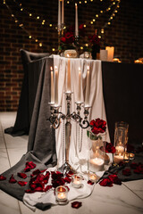 Location for surprise proposal at night. Luxury romantic date.  Decoration, flower petals, burning candles. Table setting in restaurant for the event. Candlelight for couple on Valentine's day.