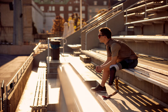 Man with a prosthetic running blade sitting outside on bleachers