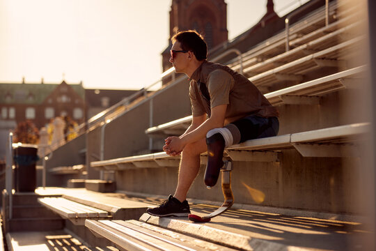 Man with a prosthetic running blade sitting on bleachers outdoors