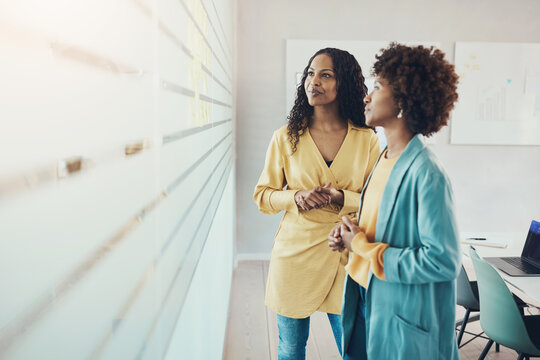 Businesswomen brainstorming together using adhesive notes on an office wall