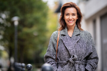 Brunette haired woman wearing tweend coat and walking outdoors in the city street on autumn day - obrazy, fototapety, plakaty