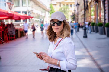 Attractive mid aged woman with smartphone walking on the street