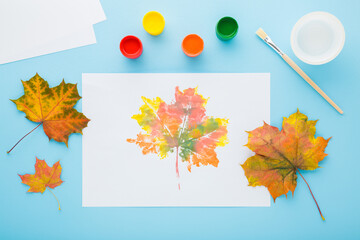 Painting and copying colorful leaf pattern with gouache color on white paper. Light blue table...