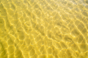 Sea water over golden sand. Glares of light on the sandy bottom. Crystal clear water on the beach.