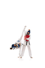 Two young girls in dobok and helmet training, practicing taekwondo poses, stances isolated over white background. Concept of martial arts, combat sport, competition, action