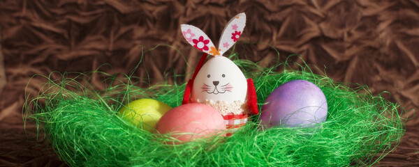 Colorful Easter eggs and bunny rabbit in green next decoration on brown copy space background banner