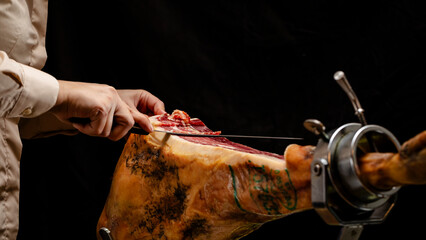 Mujer cortando delicioso jamón de cebo ibérico con cuchillo sobre fondo negro panorámico con...
