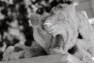 Closeup of a stone gargoyle sculpture on a wall in grayscale