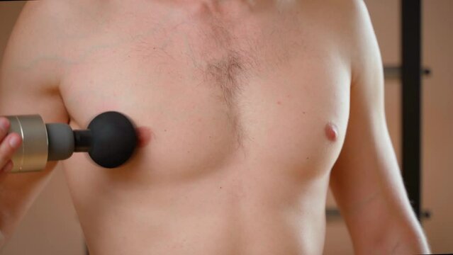 A guy gives himself a self-massage of the pectoral muscle with a percussion massager, close-up. Chest massage after training