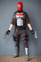 Male cosplayer in a costume with a red helmet, leather jacket, and guns
