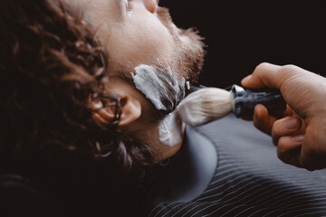 Closeup barber shaving man with sharp steel razor, barbershop warm retro old toning