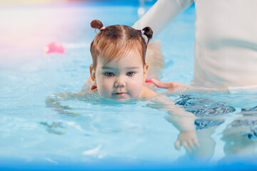 Fototapeta na wymiar Cute happy baby girl swimming with instructor in pool. Concept health care sport for kid