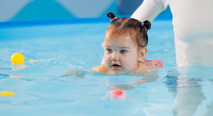 Fototapeta na wymiar Cute happy baby girl swimming with instructor in pool. Concept health care sport for kid