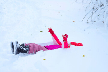 Happy kid  lying in snow and playing  in winter nature