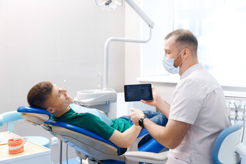 Dentist use digital tablet for client patient man looking at screen in modern dental clinic