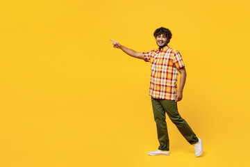 Full body side view smiling happy young Indian man he wears shirt casual clothes walking going point finger aside on area isolated on plain yellow color background studio portrait. Lifestyle concept. - obrazy, fototapety, plakaty