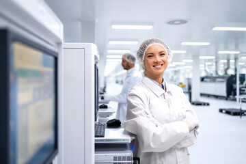 Portrait of smiling female employee standing by automated production machine in factory.