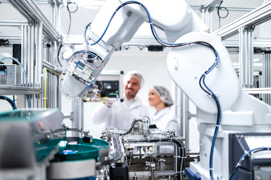 Factory robotic arm operating production process and engineers working on the computer.