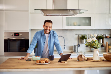 Portrait of a cheerful male online content creator leaning on his hands on a kitchen counter with...