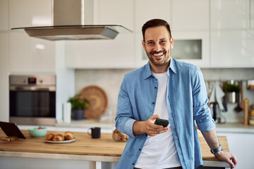 Portrait of an enthusiastic young adult real estate agent holding a cellphone while leaning on a...