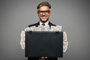 Adult rich happy employee business man corporate lawyer he wears classic formal black suit shirt tie work in office hold of cash money in case for dollar banknotes isolated on plain grey background. - obrazy, fototapety, plakaty