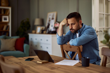 A stressed freelance man sighing and looking at his tablet for work while sitting backwards on a chair.