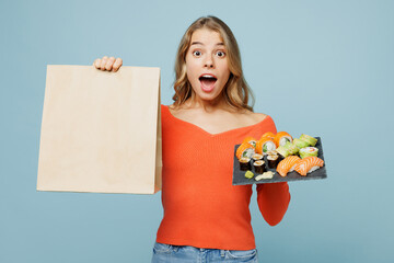 Young surprised woman wear orange casual clothes hold brown clear blank craft paper takeaway bag...