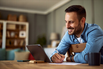 A smiling adult man taking notes while watching an educational video on his tablet.